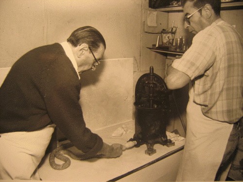 Two men making sausage by hand with a cast-iron stuffer